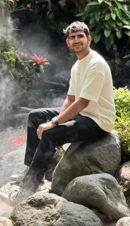 Vishesh Gupta sitting on a rock beside a misted koi pond